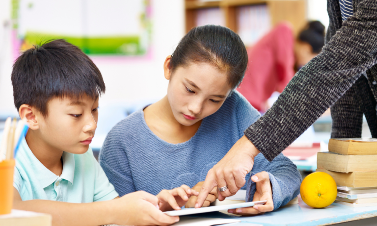 Students using a tablet with teacher guidance in a classroom, supporting digital learning, educational technology, and interactive education